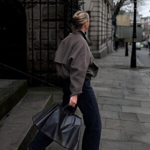 woman in rainy cobbled streed carrying black bag with a black rain cover over the top