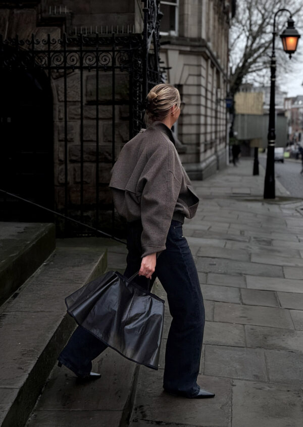 woman in rainy cobbled streed carrying black bag with a black rain cover over the top